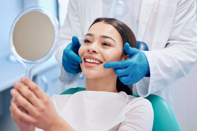 Mujer viendo con un espejo como quedó su limpieza dental.