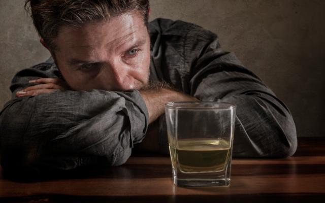 hombre apoyado en mesa con vaso de alcohol delante