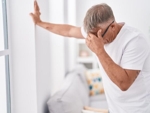 Hombre con mareo al levantarse apoyado en la pared de su casa